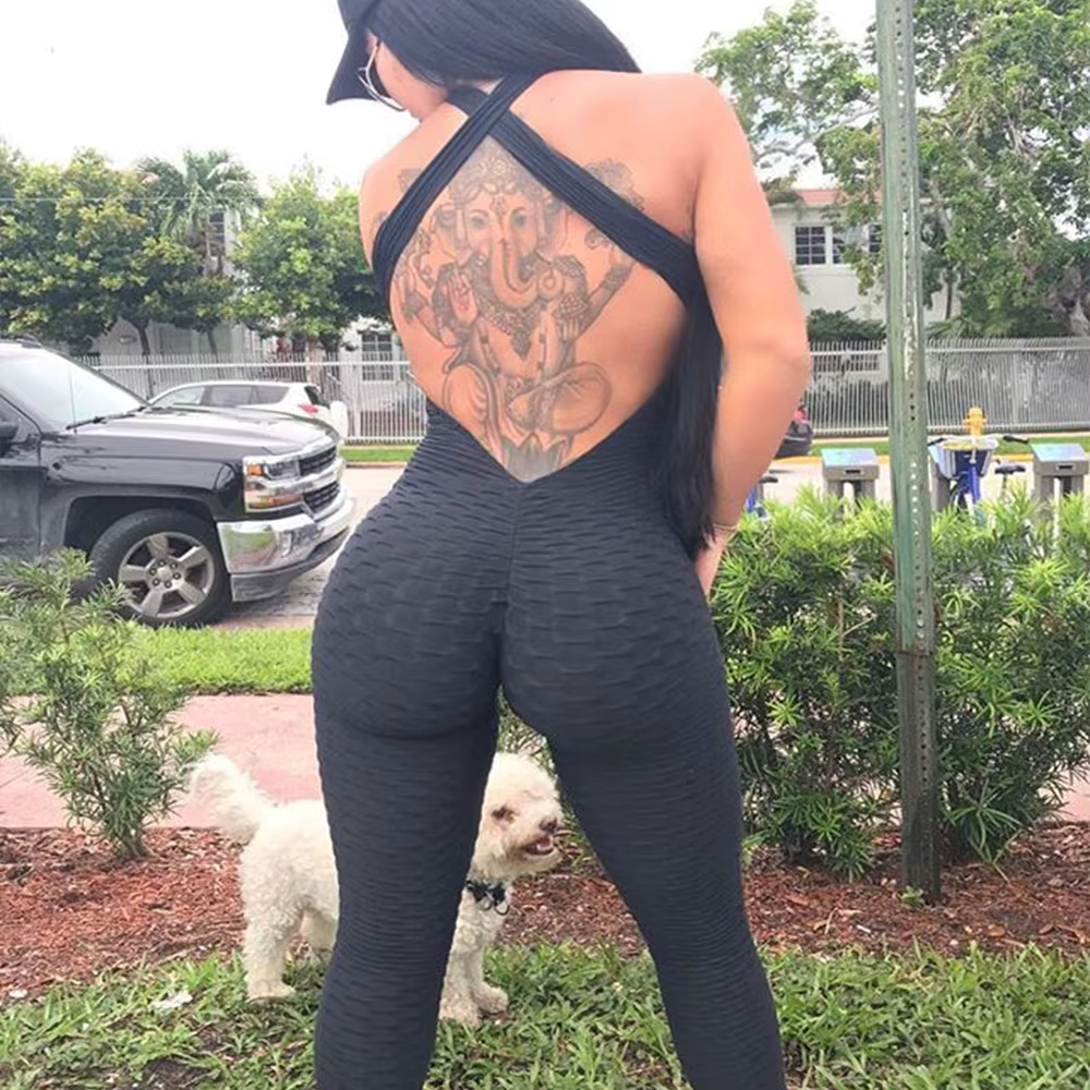 Woman in a stylish sleeveless backcross bodysuit outdoors, showcasing a tattoo and walking a small dog.