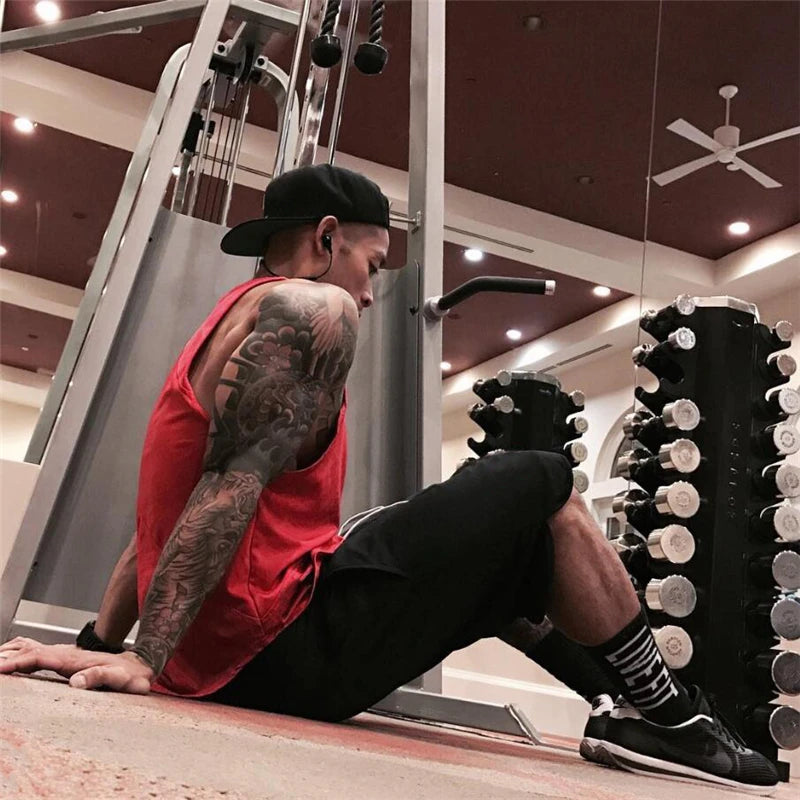 Man in red tank top working out in gym, using equipment with weights, showcasing fitness training and bodybuilding.