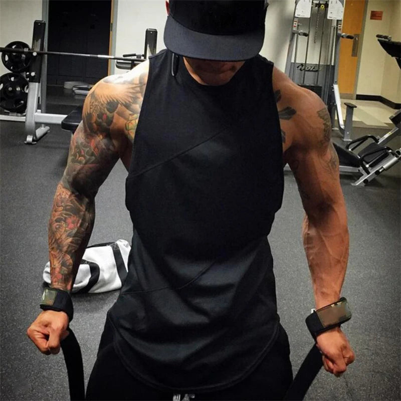 Man wearing a sleeveless black gym tank top with tattoos, showing muscles in a fitness environment.