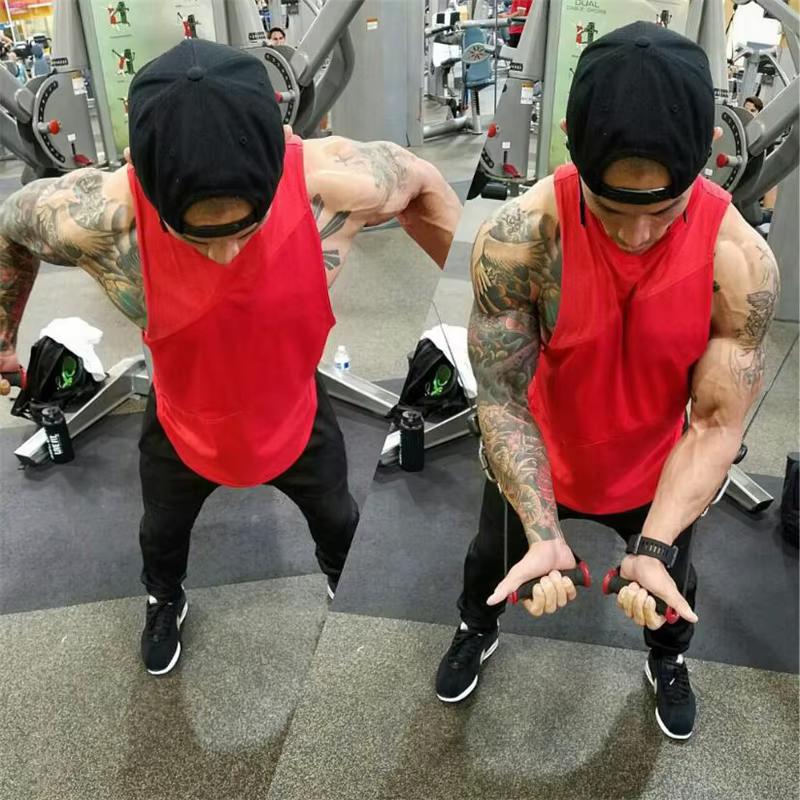Muscular man in red sleeveless tank top exercising with weights in a gym, showcasing strength and fitness.