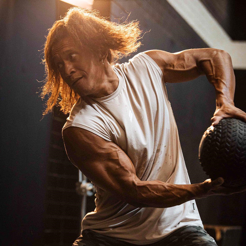 Athlete in white tank top performing strength training with heavy ball in gym setting.