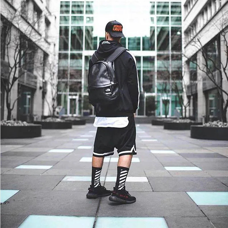 Stylish man wearing black mesh basketball shorts and a backpack in a modern urban setting.
