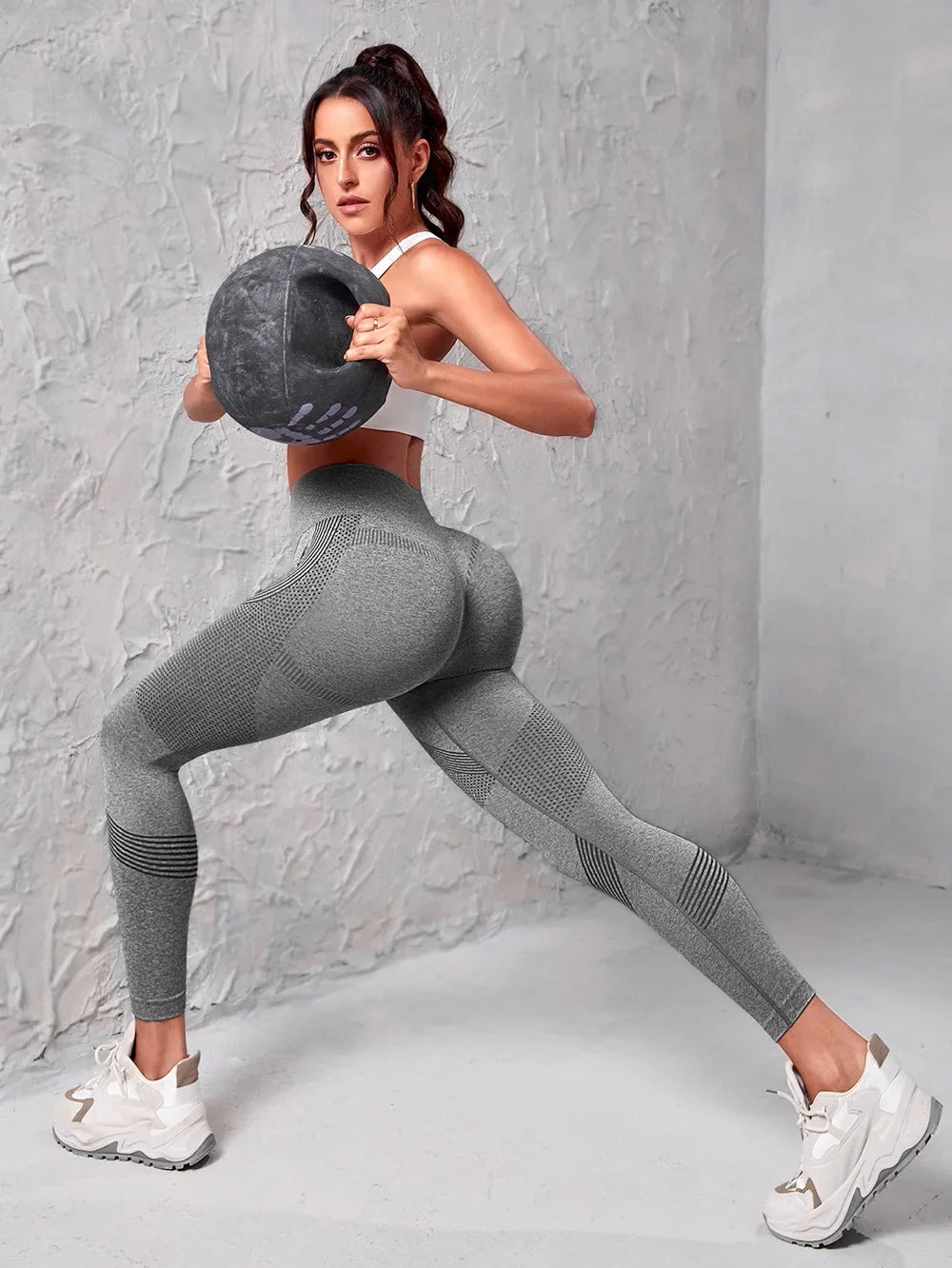 Model demonstrating Seamless Butt-Lift High Waist Leggings while exercising with a weight ball in a stylish fitness outfit.