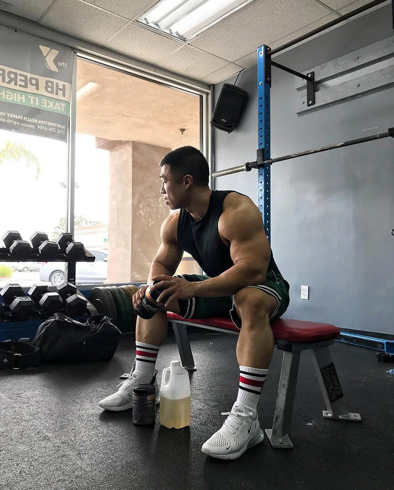 Fit man resting on a bench in a gym, wearing basketball shorts and athletic gear, emphasizing strength and fitness.