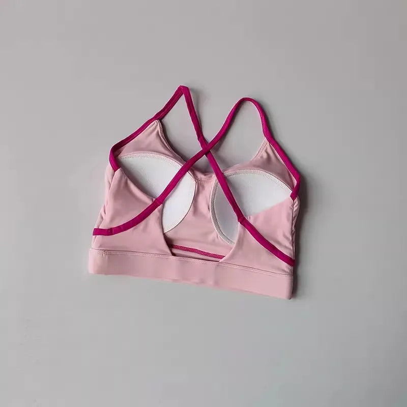 Light pink sports bra with crisscross straps, ideal for yoga and fitness activities, made from breathable fabric.