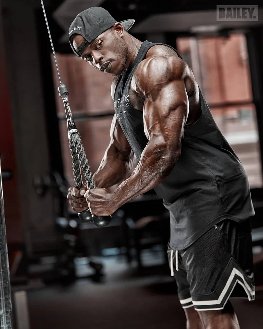 Muscular man working out with cable machine in gym, showcasing strength and fitness in athletic wear.