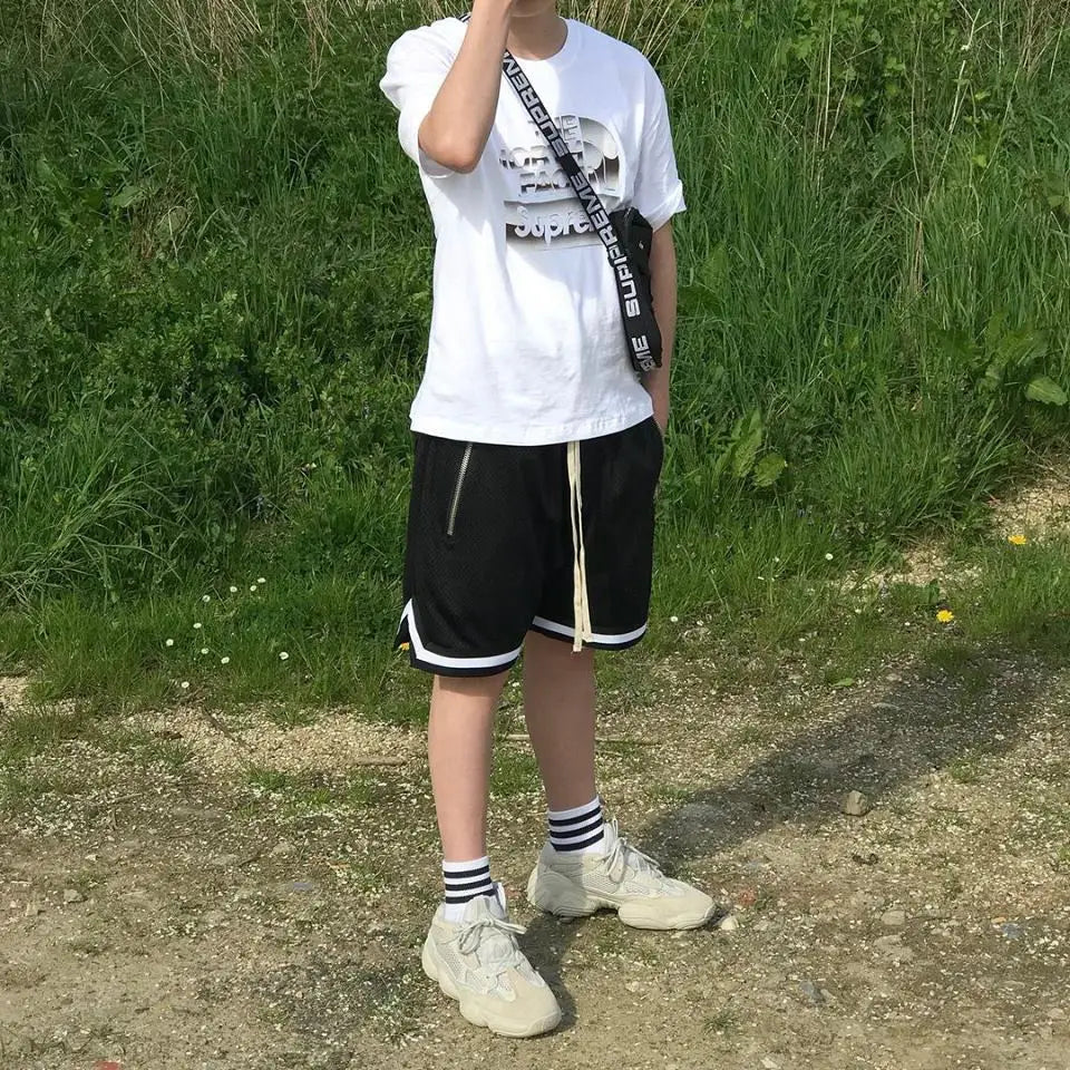 Casual outfit featuring a person in black mesh basketball shorts and a white graphic t-shirt on a sunny day.