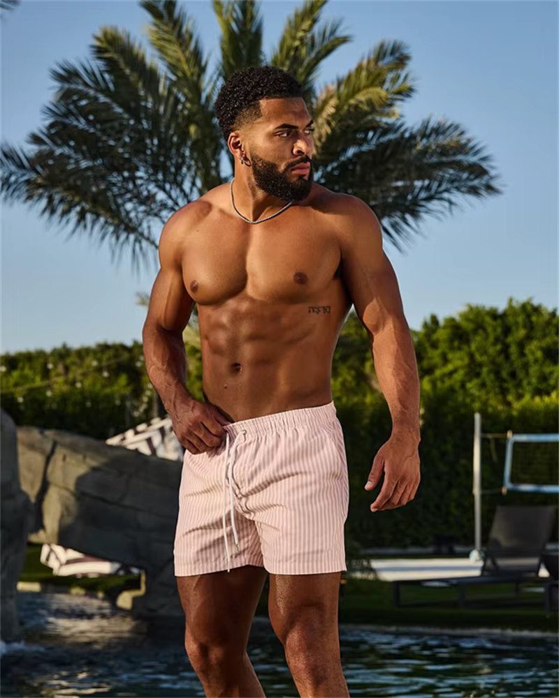 Man wearing casual striped shorts, showcasing a stylish look by the poolside, surrounded by palm trees.