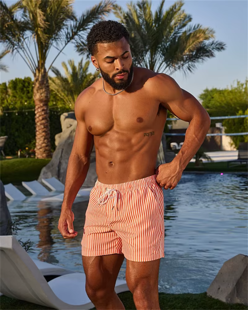 Man in stylish casual shorts by the pool surrounded by palm trees, exemplifying outdoor leisure wear.