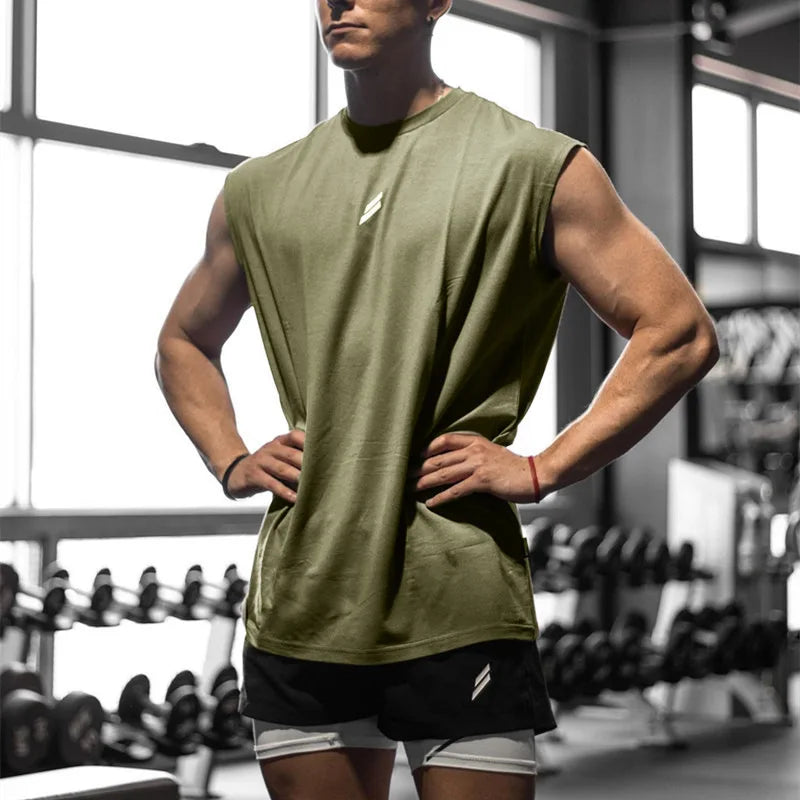 Muscular man in olive green sleeveless tank top showcasing summer fitness apparel in gym setting.