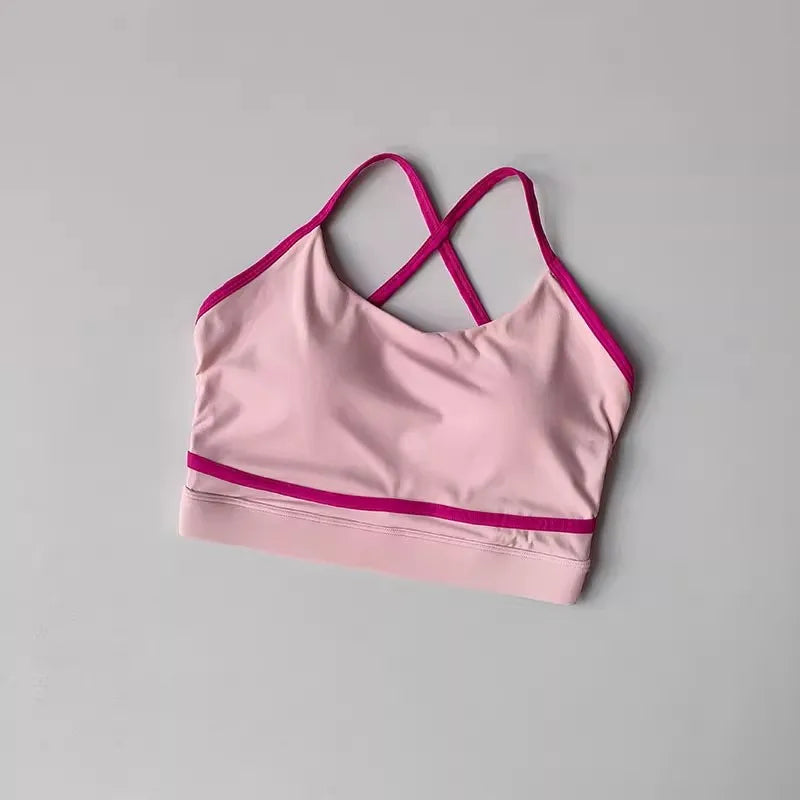 Pink women's sports bra with crisscross straps and contrasting trim, perfect for yoga and activewear.