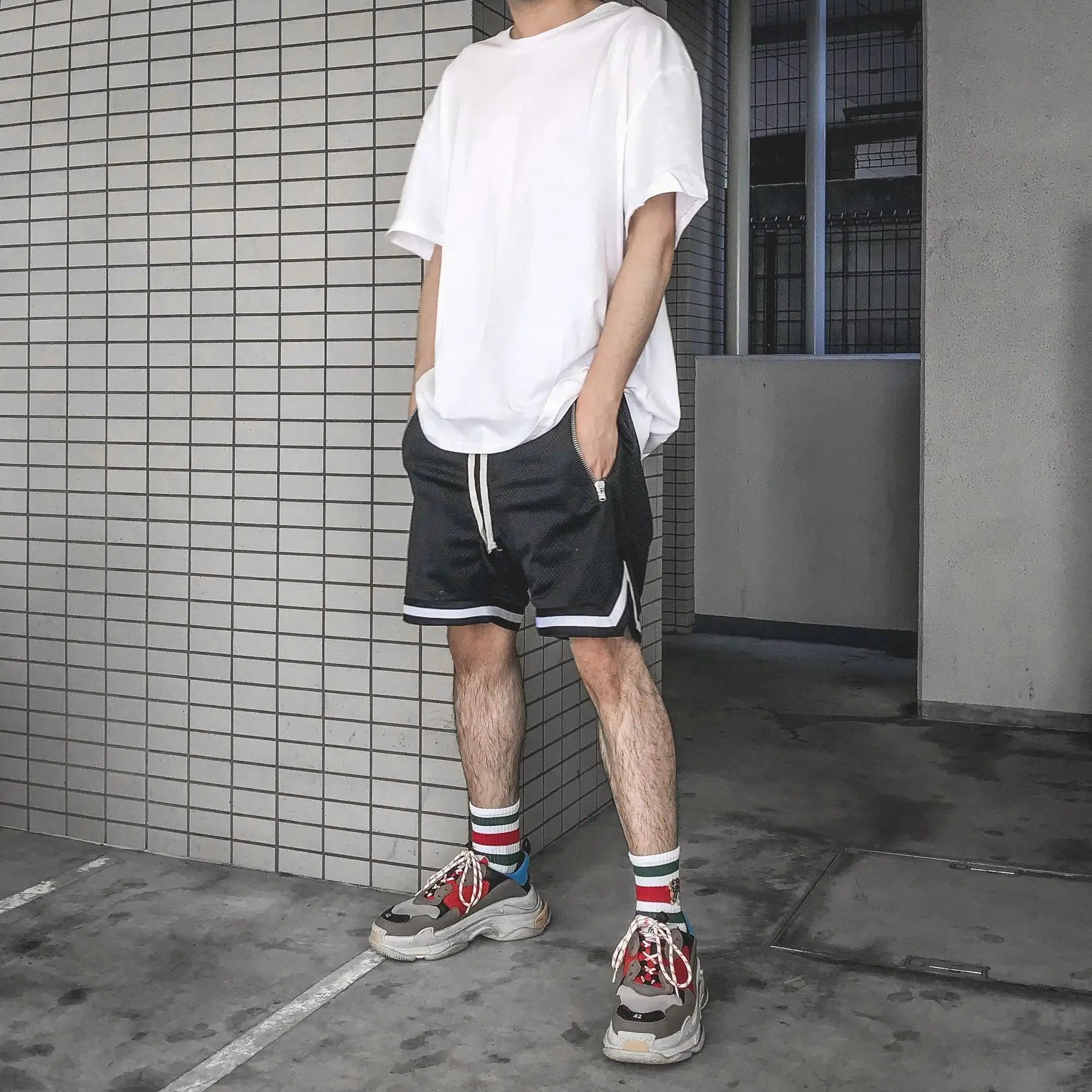 Man wearing black mesh basketball shorts and white tee in urban setting, showcasing sporty style and comfort.