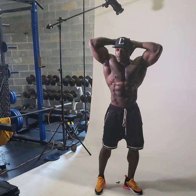Muscular man posing in men's mesh basketball shorts in a gym setting with weights in the background.