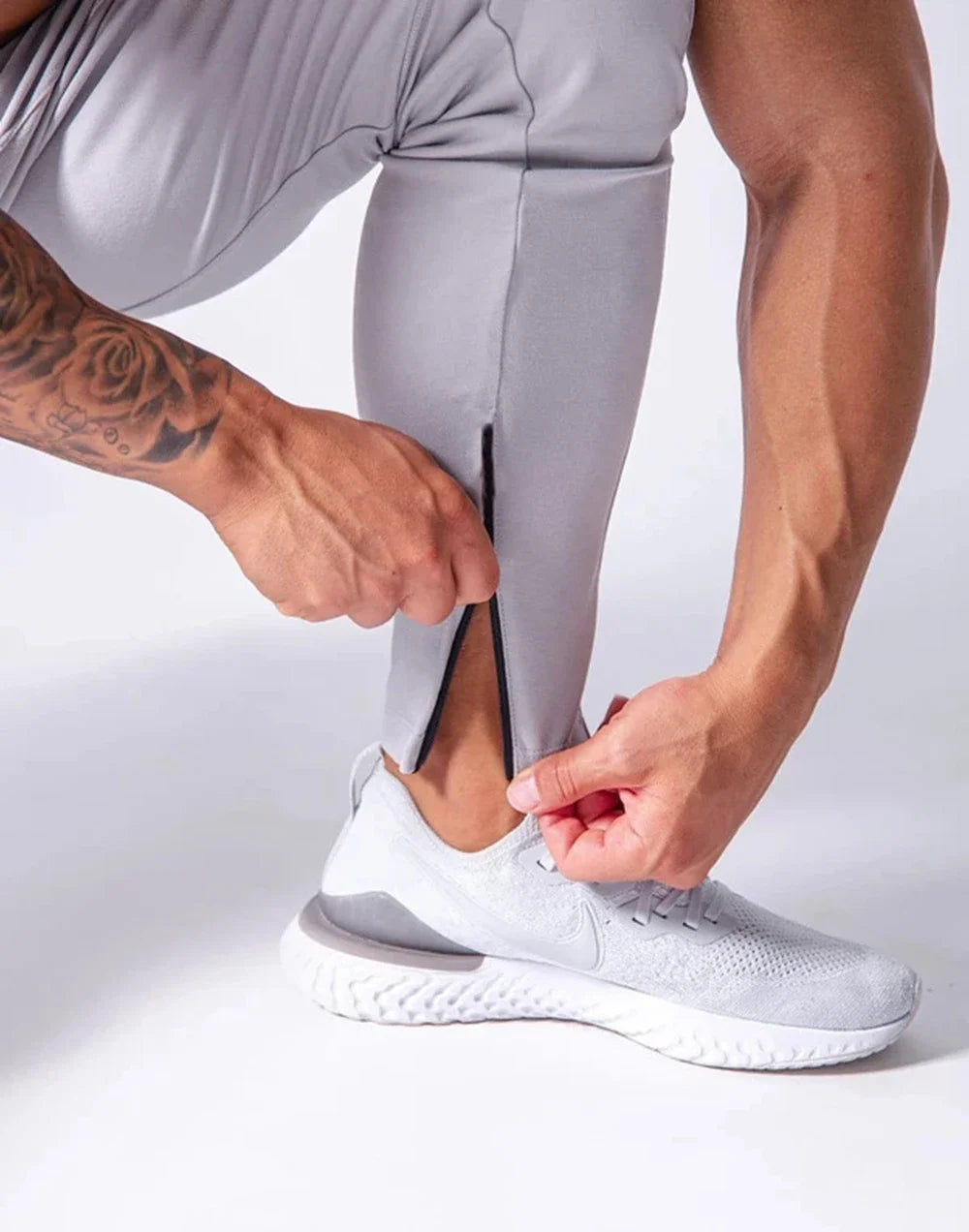 Man adjusting the zipper on gray men's performance training pants, showcasing flexibility and comfort for workouts.