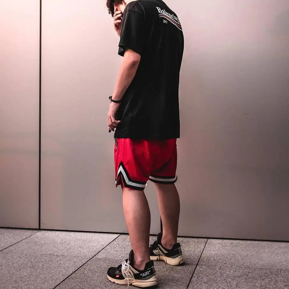 Man wearing red mesh basketball shorts and a black t-shirt, showcasing sporty style and comfort.