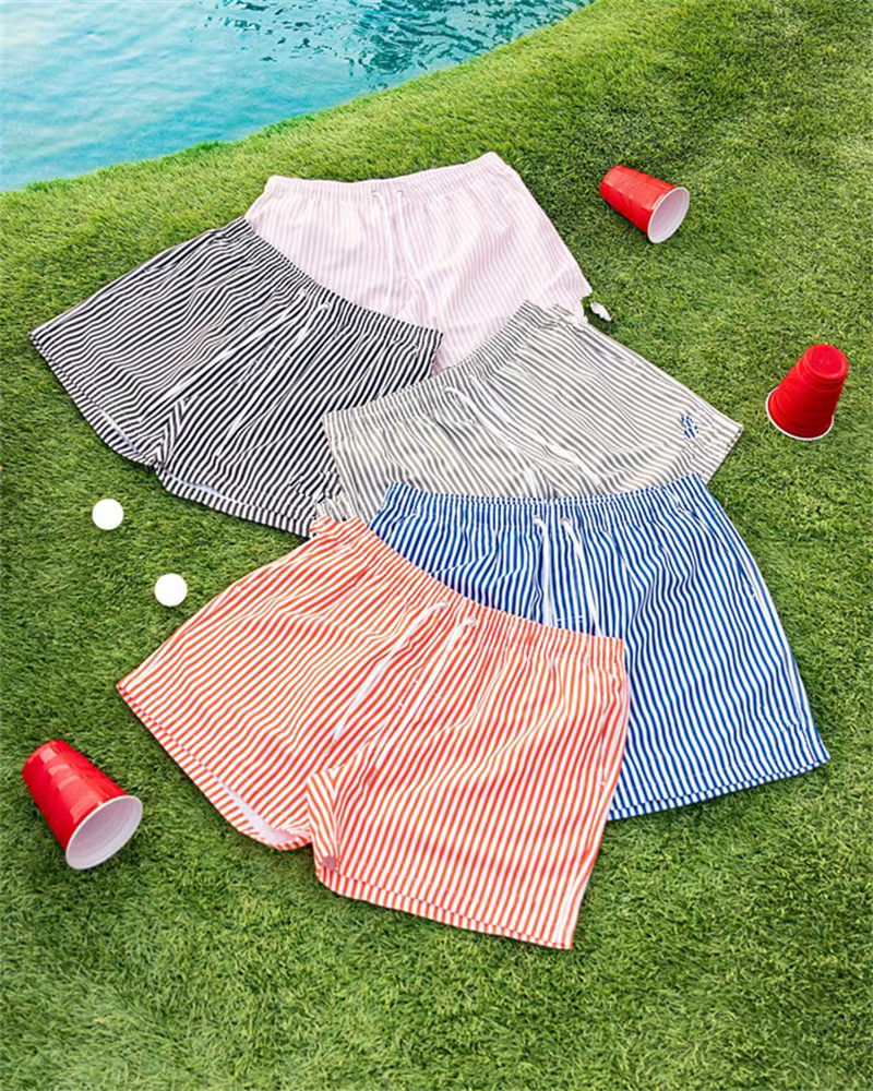 Men's casual sports outdoor shorts in various colors and patterns on grass near a pool.