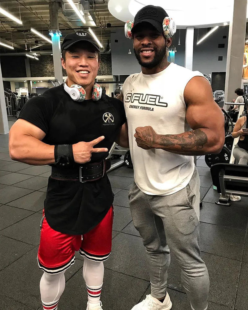 Two men posing in a gym, wearing workout gear and headphones, showcasing fitness and friendship.
