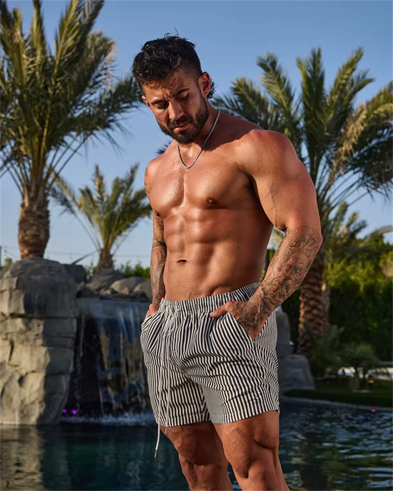 Man wearing striped casual sports shorts by a poolside with palm trees in the background, showcasing a stylish outdoor look.