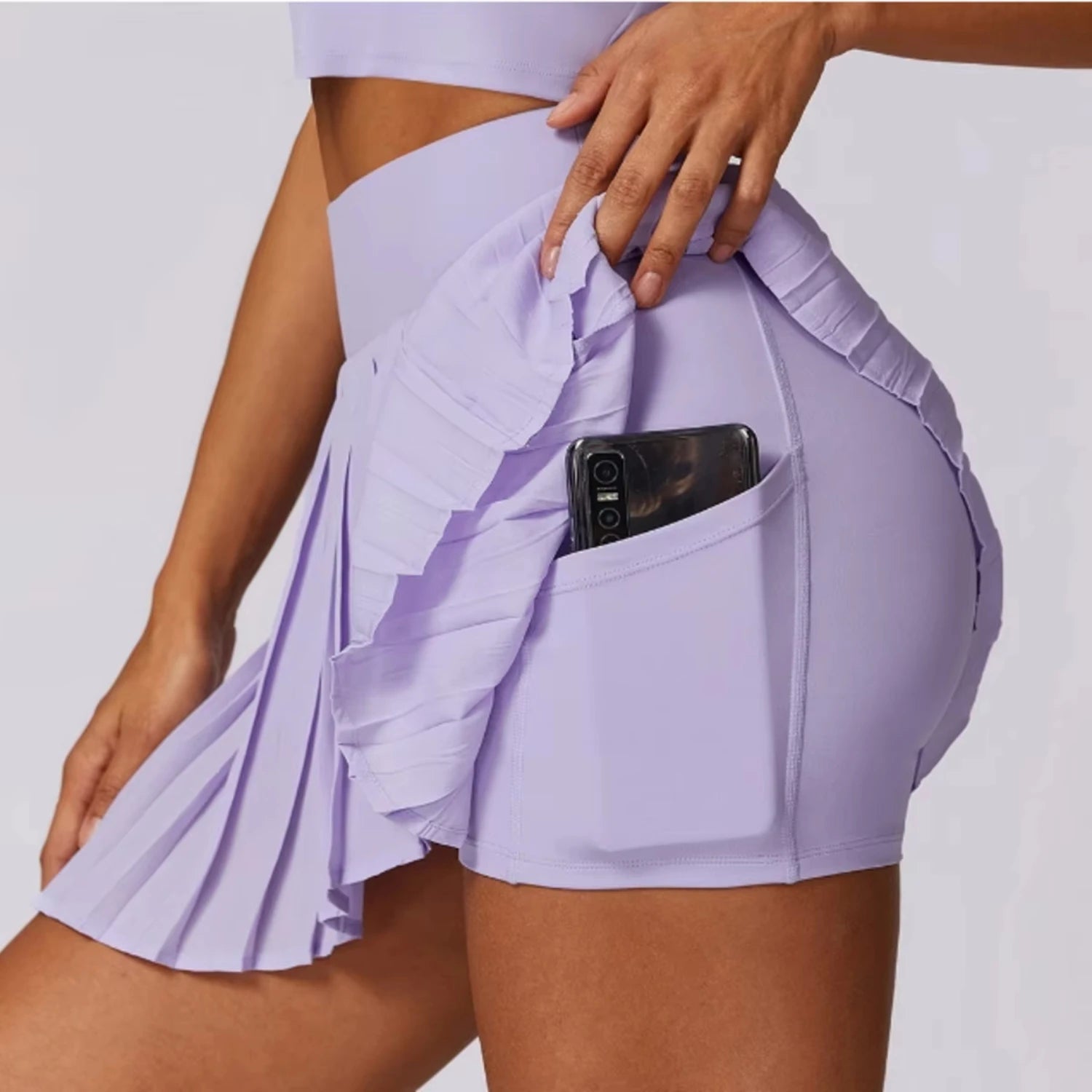 Side view of a woman wearing a lavender safe tennis skirt with pocket shorts, showcasing ruffle details and a secure phone pocket.