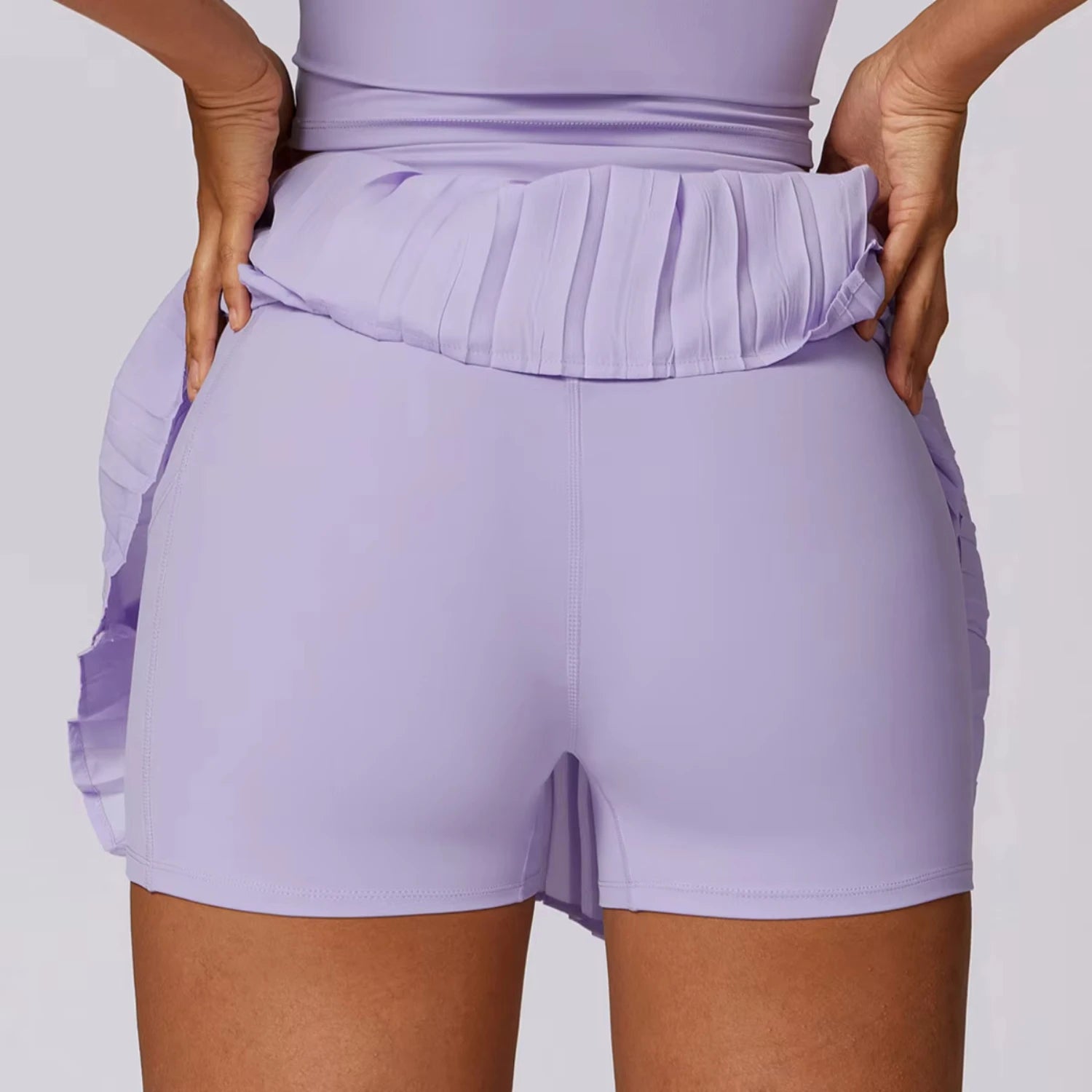 Back view of a model wearing a lilac tennis skirt with ruffle detailing and built-in pocket shorts.