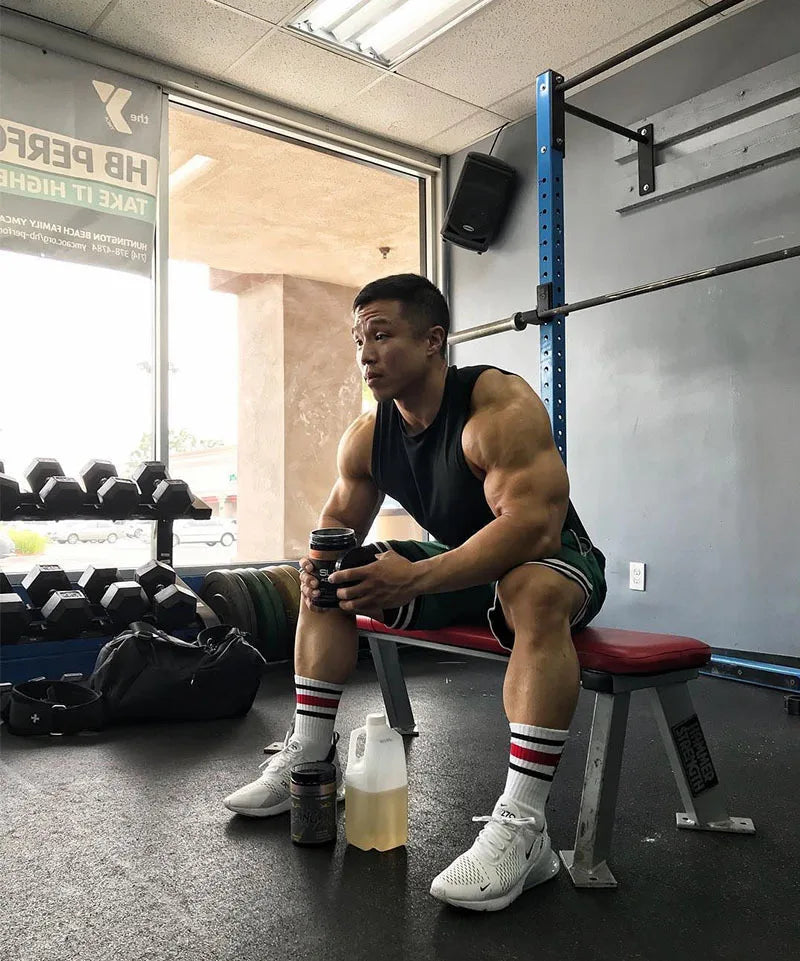 Fit man resting on a bench in a gym, showcasing strength and athleticism, with workout gear and weights nearby.
