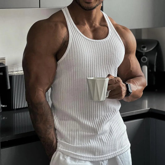 Man in a white sleeveless vest holding a mug in a modern kitchen, highlighting casual summer style.
