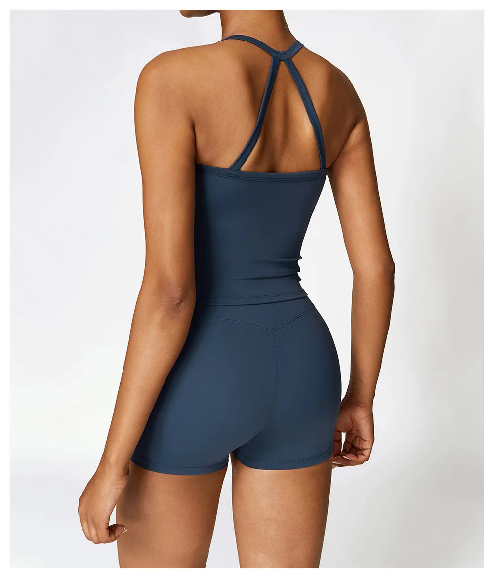 Back view of a woman in a navy blue cross back sports bra and shorts, showcasing stylish activewear design.