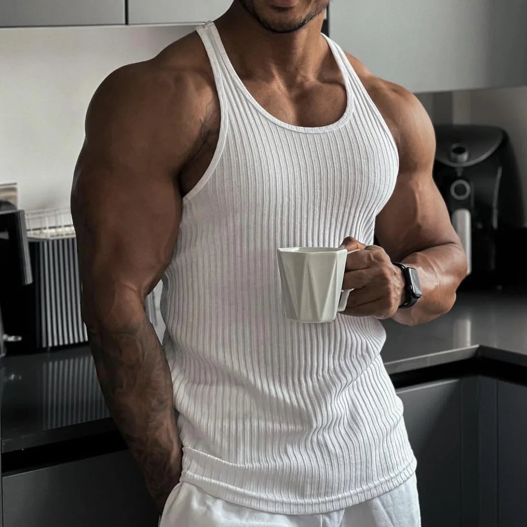 Man in a white sleeveless vest holding a mug in a modern kitchen, highlighting casual summer style.